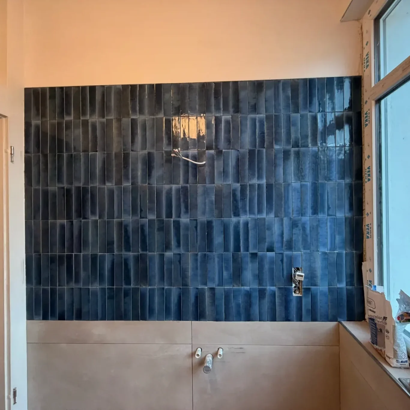 Badezimmer mit blauen Fliesen, Fenster und handgefertigtem Waschbecken.